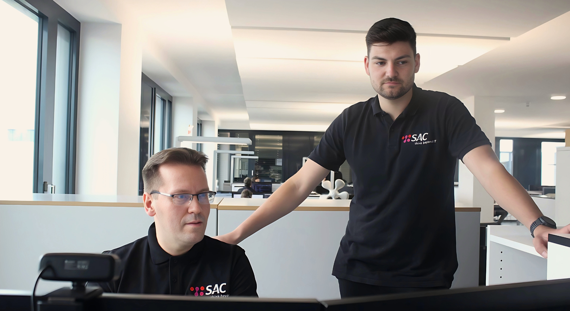 Foto von zwei SAC Mitarbeitern welche sich gemeinsam vor drei Bildschirmen über IT-Technische Probleme austauschen