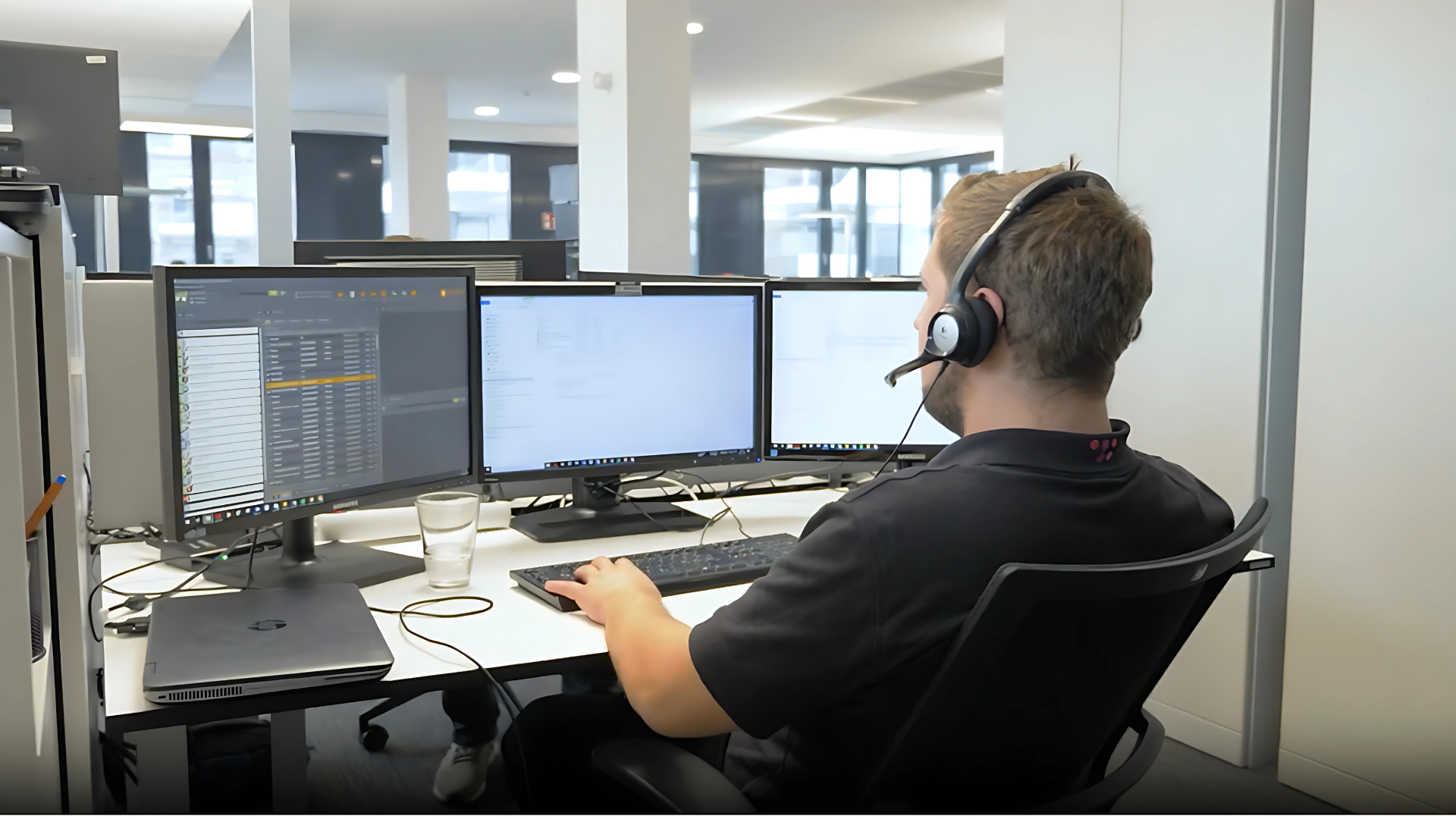 Ein SAC Mitarbeiter der an einem Schreibtisch mit mehreren Bildschirmen sitzt und über Headset einem Kunden bei einem IT-Problem hilft.