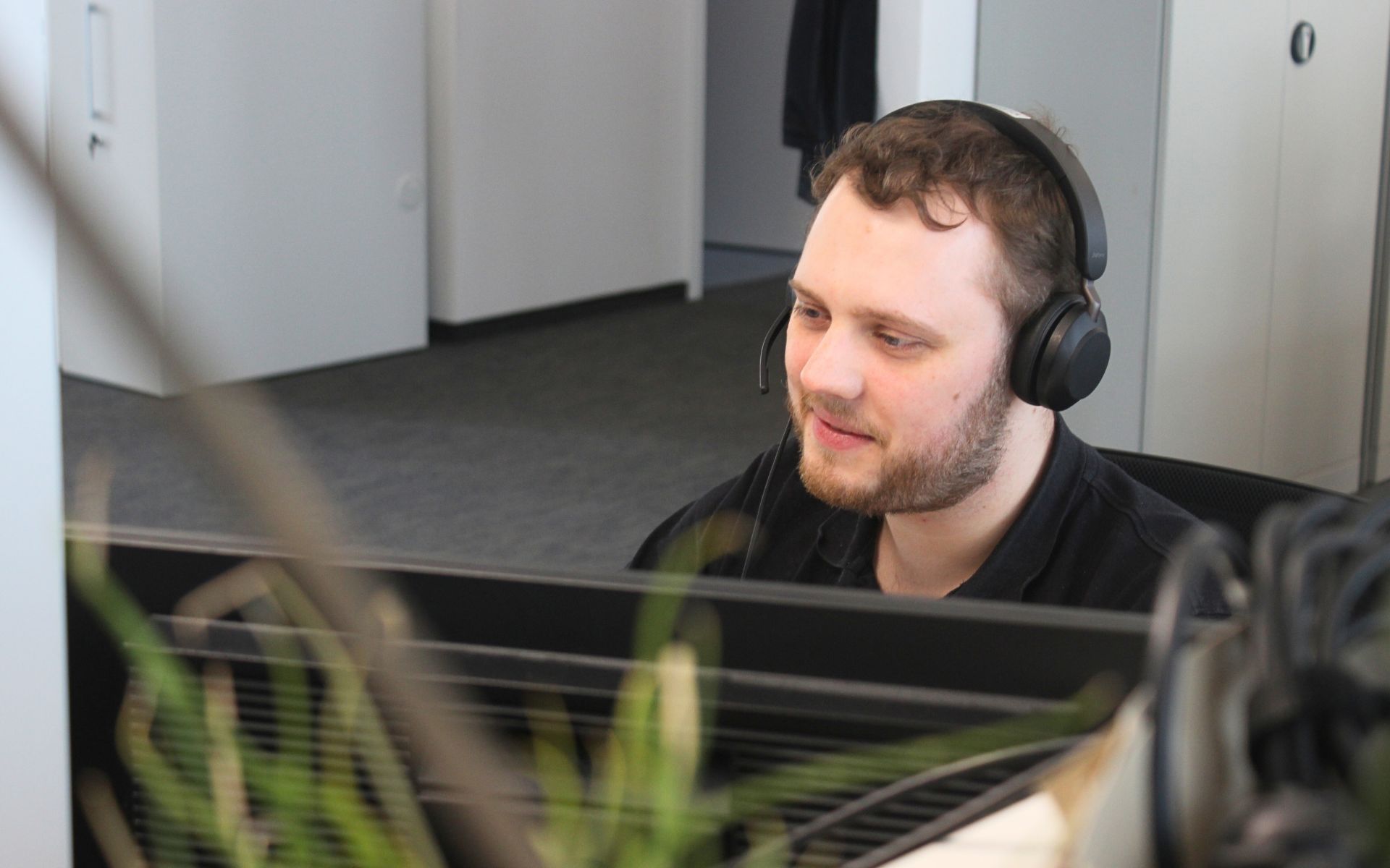 sac_foto_service-desk-mitarbeiter Ein Foto von einem IT-Mitarbeiter. Er arbeitet im IT User Support. Er hilft gerade einem Kunden über remote Support beim lösen eines technischen Problems.